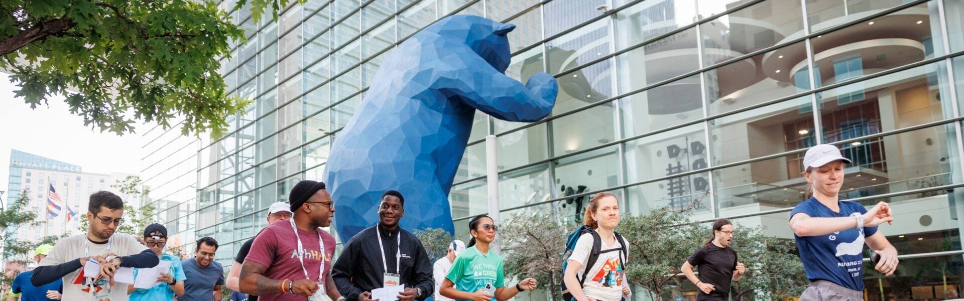 Conference attendees jog together outdoors near a large blue bear sculpture during a group fun run event.