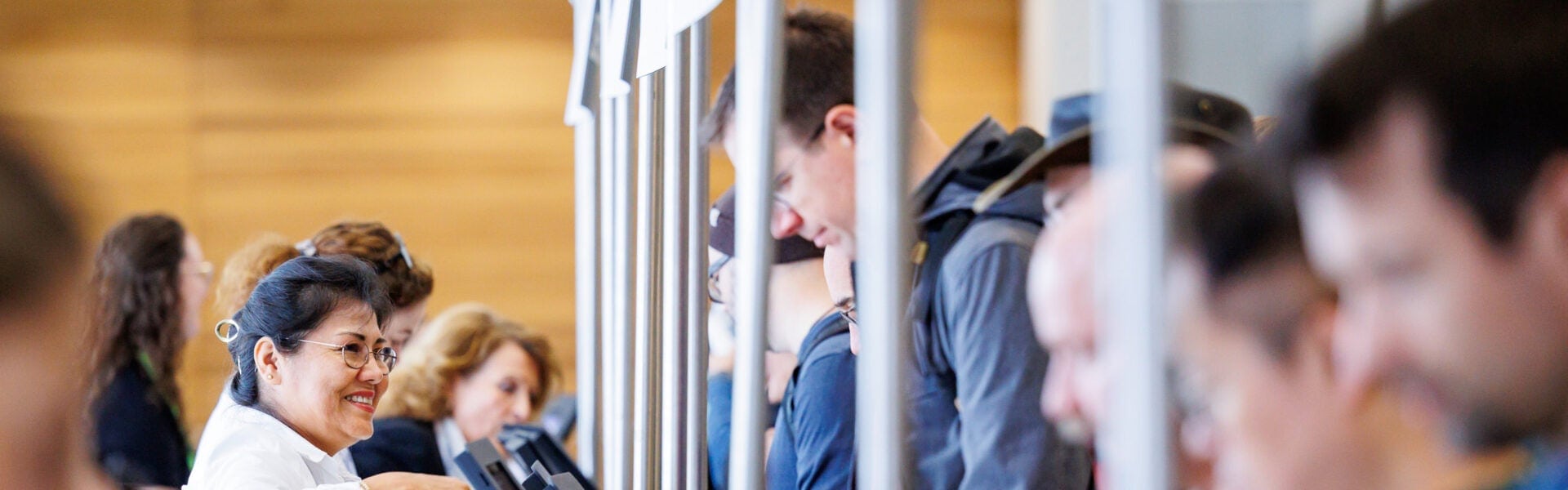 Smiling staff member assisting attendees at a busy registration counter with people waiting in line