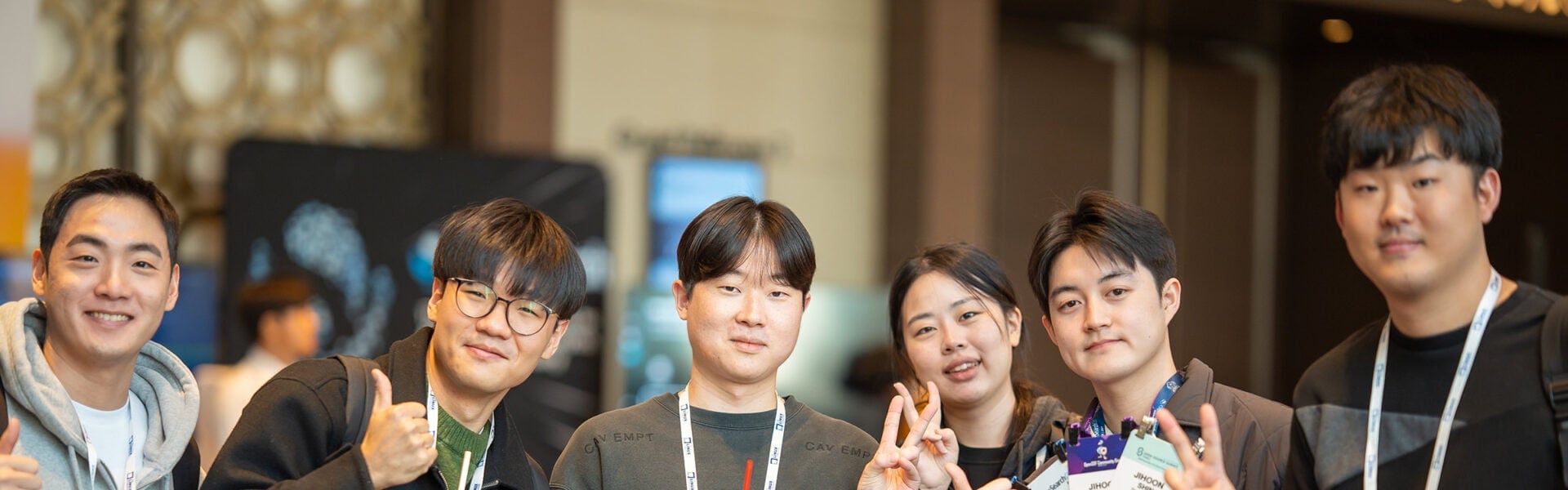 Group of conference attendees smiling at the camera, some giving thumbs up and peace signs while wearing event badges