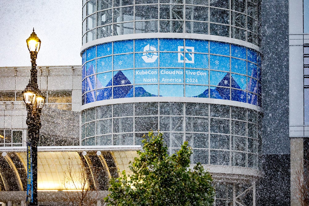 Snow falls outside a convention center displaying a KubeCon + CloudNativeCon North America 2024 banner.
