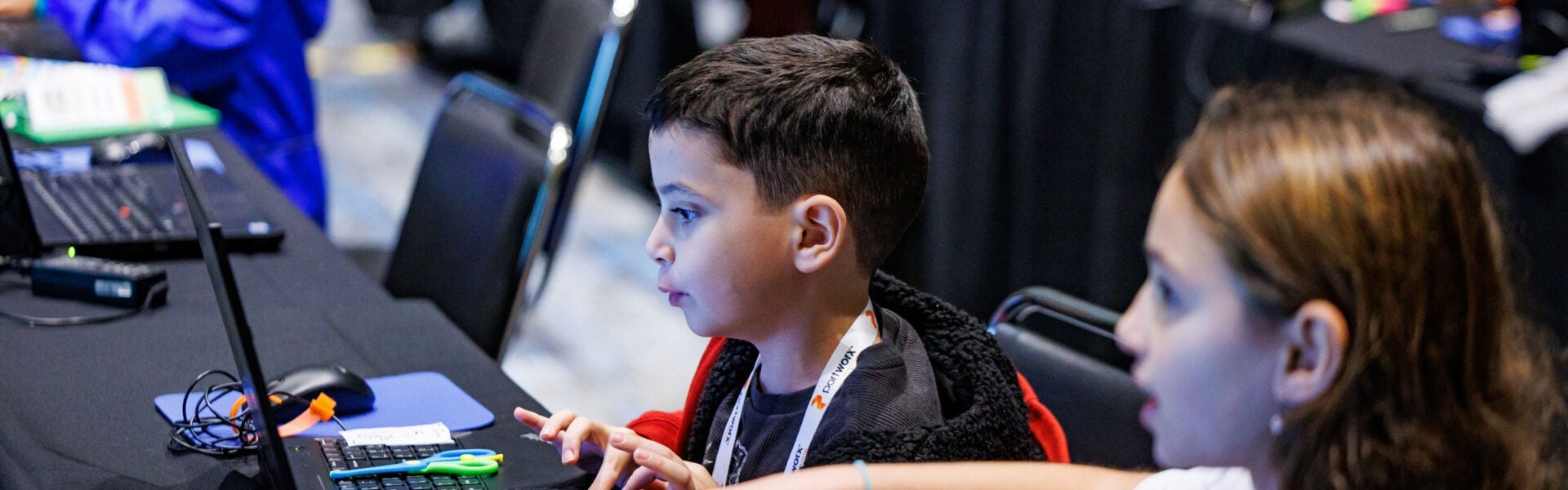 Children engage with computers during a hands-on learning session at a conference kids’ program.