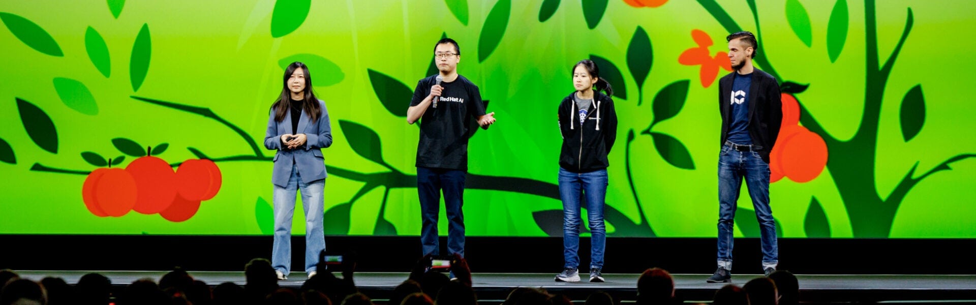 Four speakers stand on stage presenting during a conference keynote.