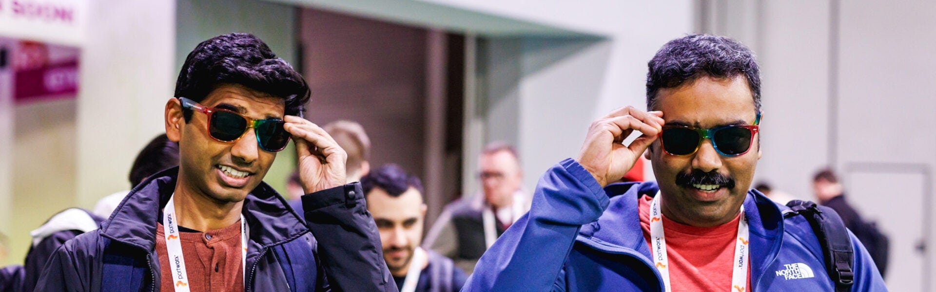 Two conference attendees smile while putting on colorful sunglasses.