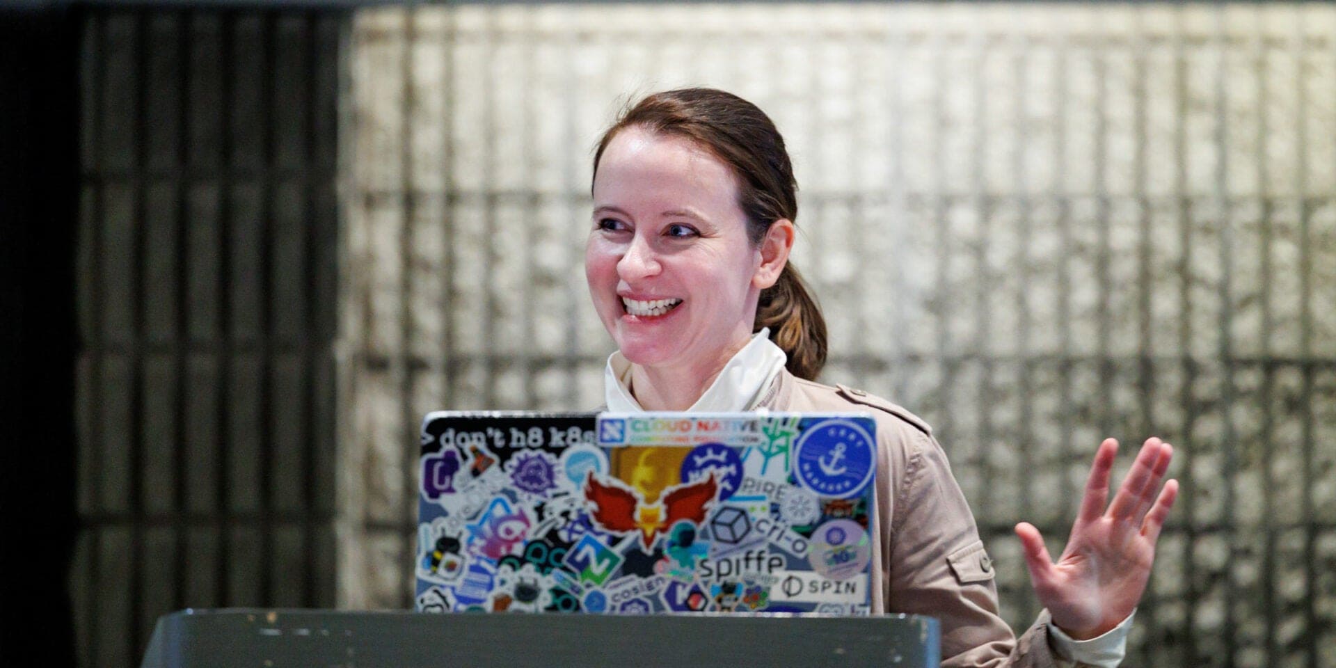 Speaker smiles while presenting from a laptop covered in open source stickers.