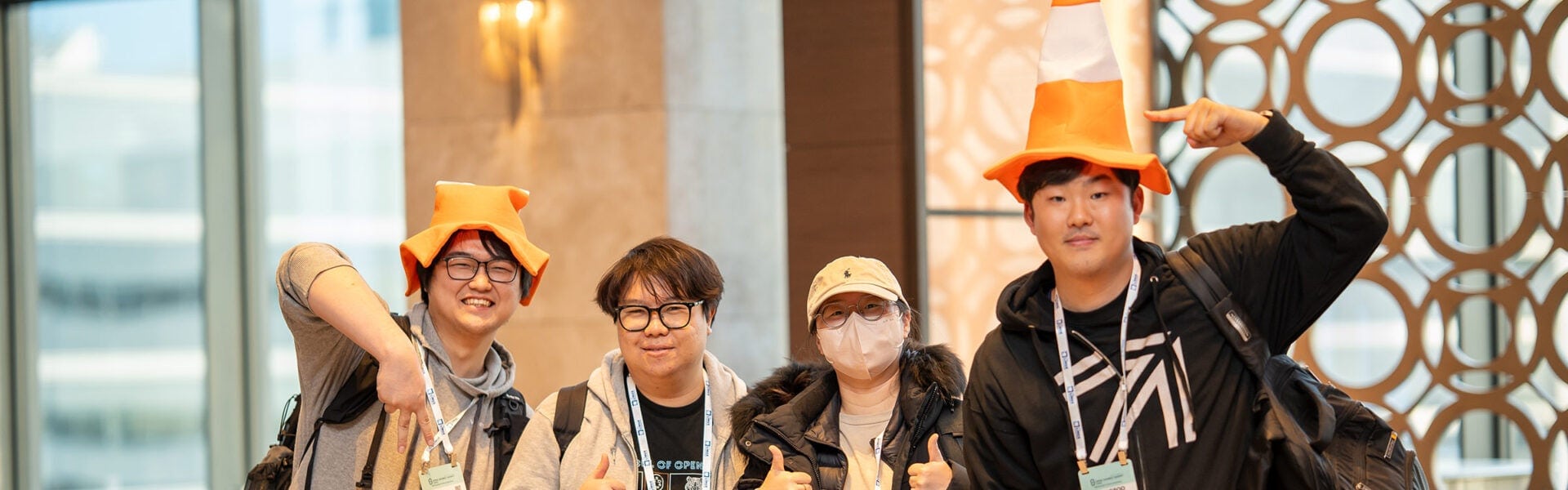 Group of Open Source Summit attendees posing together indoors, two wearing orange cone-shaped hats and giving thumbs up while smiling at the camera.
