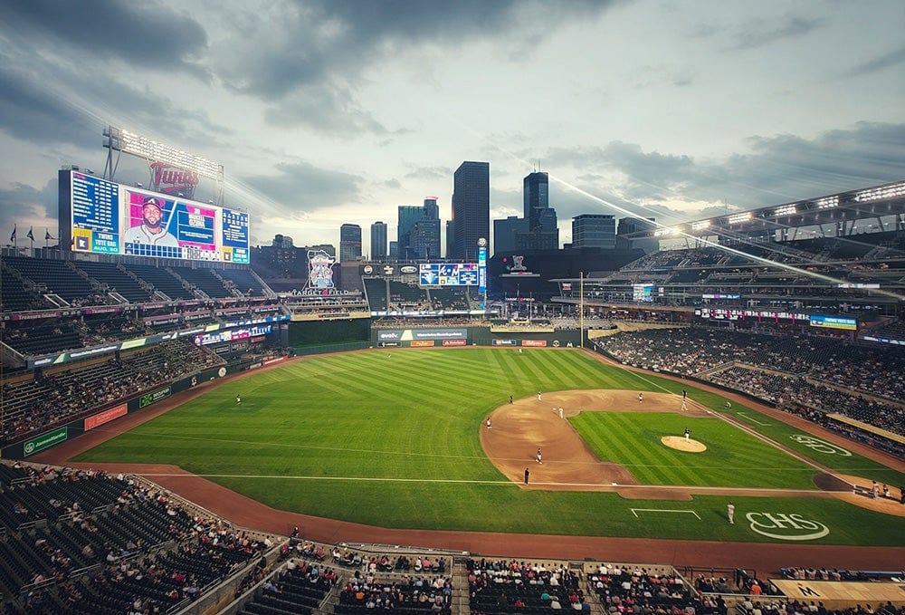 A wide, slightly elevated, twilight view of a baseball stadium with a game in progress.