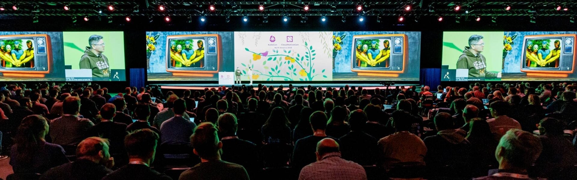 Large audience watches a keynote presentation on a brightly lit conference stage.