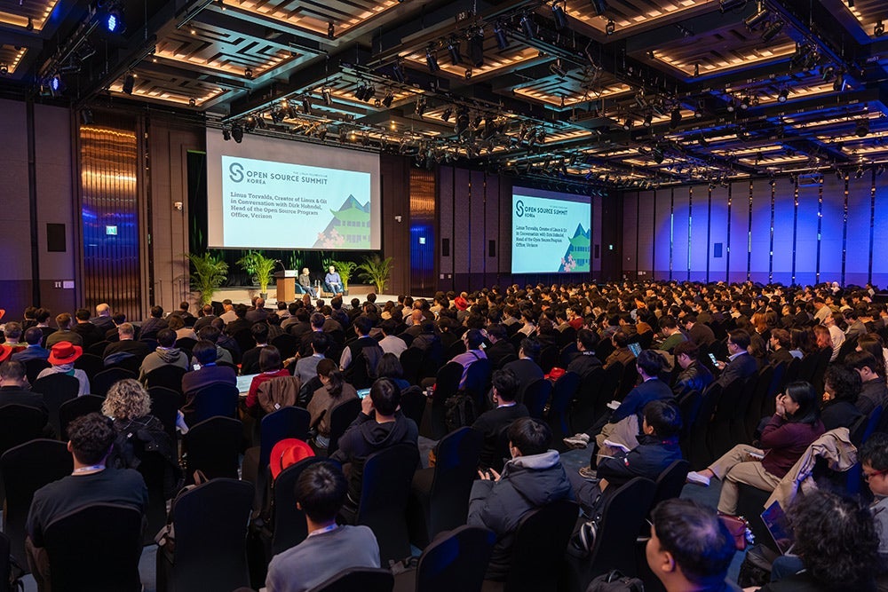 Full conference hall with a large audience watching speakers on stage during a presentation