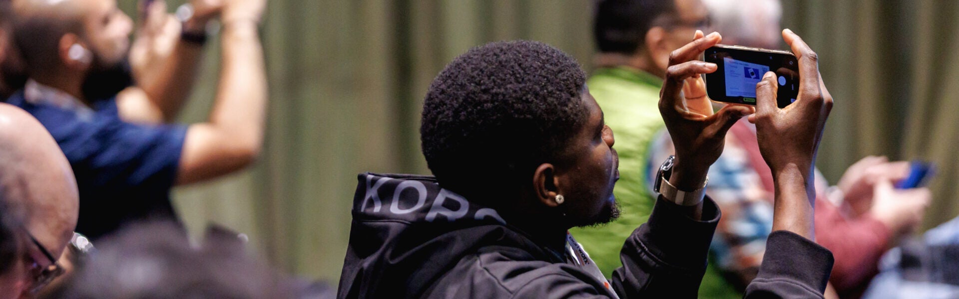 Conference attendee holding up a smartphone to take a photo during a presentation