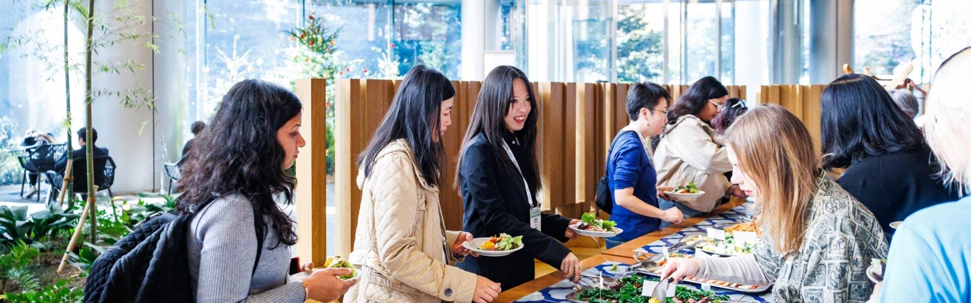 Conference attendees serve themselves from a buffet lunch while networking in a bright, modern dining area.