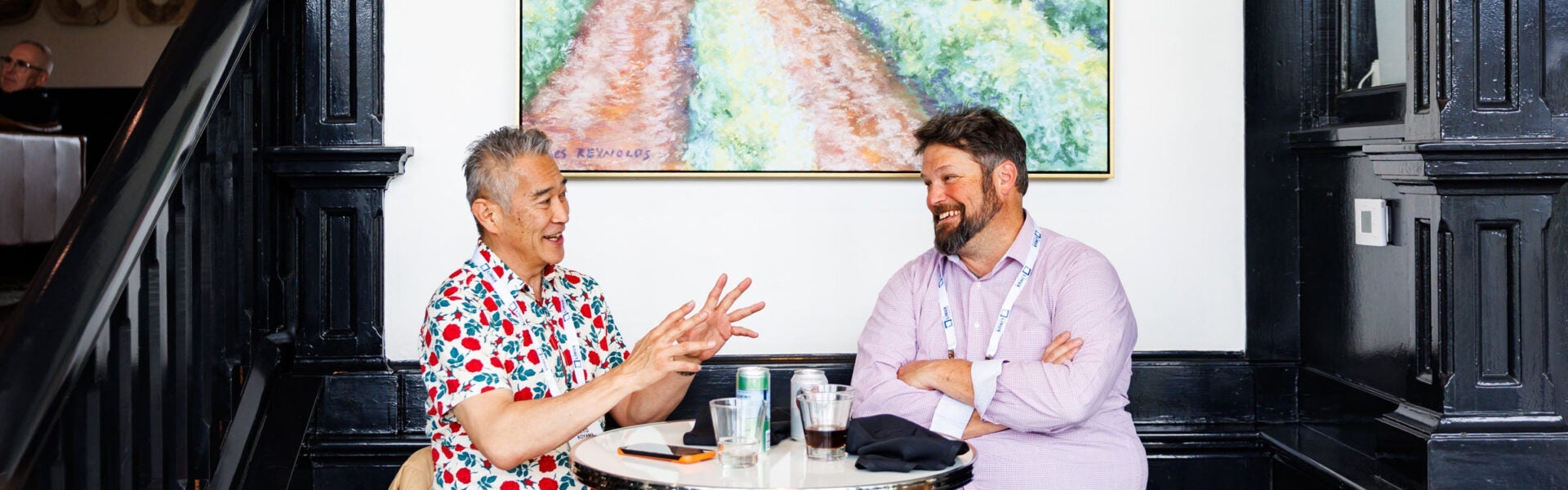 Two conference attendees seated at a small table, smiling and talking over drinks.
