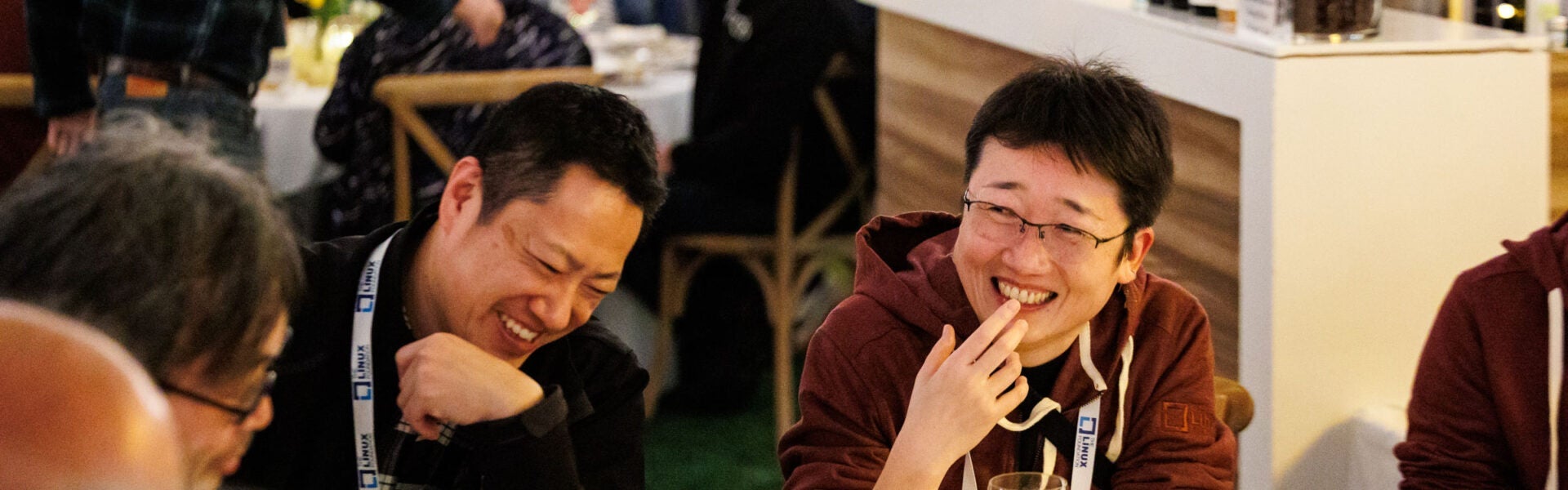 Conference attendees seated together around a table, smiling and laughing during a conversation.