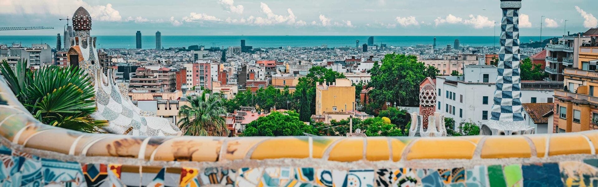 Panoramic view of Barcelona overlooking the city and Mediterranean Sea, with colorful mosaic architecture in the foreground.