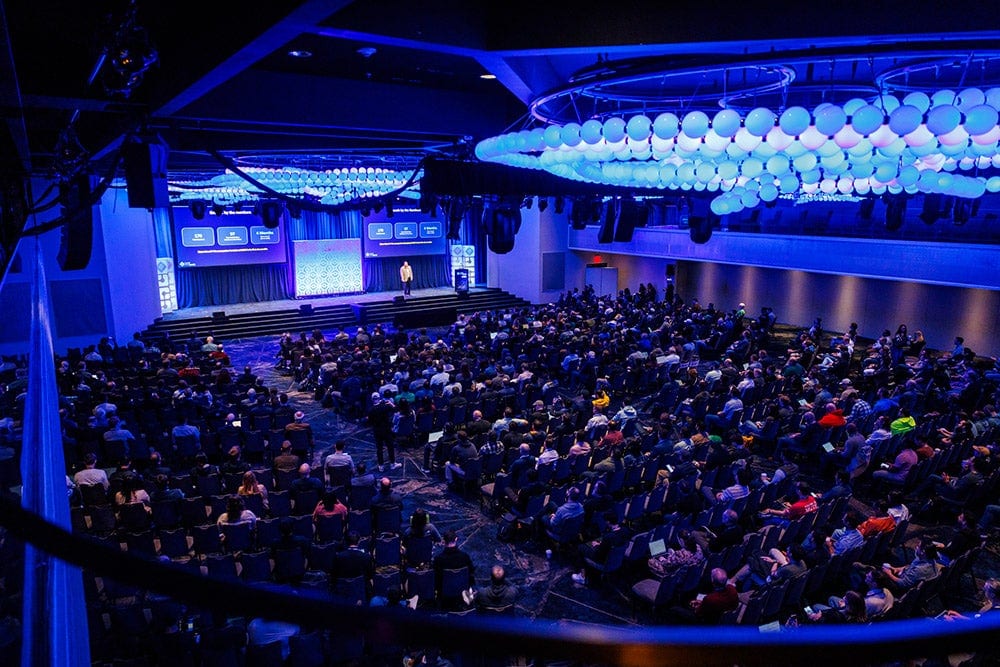Large conference audience seated in a ballroom, watching a presentation on stage.