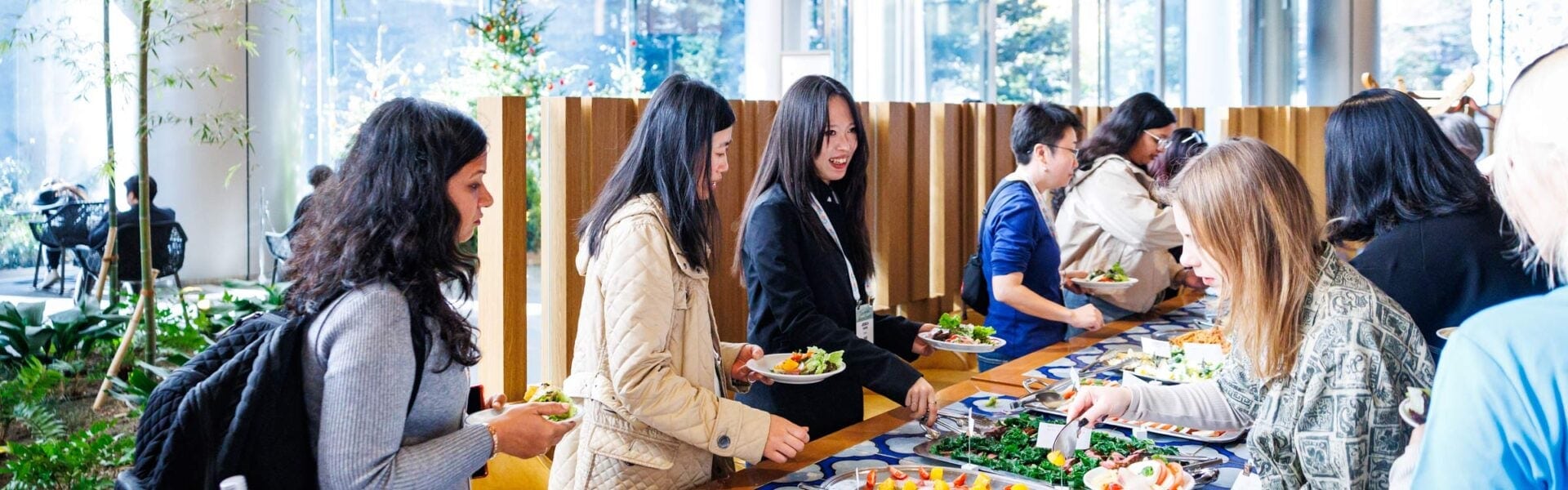 A group of women standing along a buffet table selecting food and conversing during a networking lunch event.